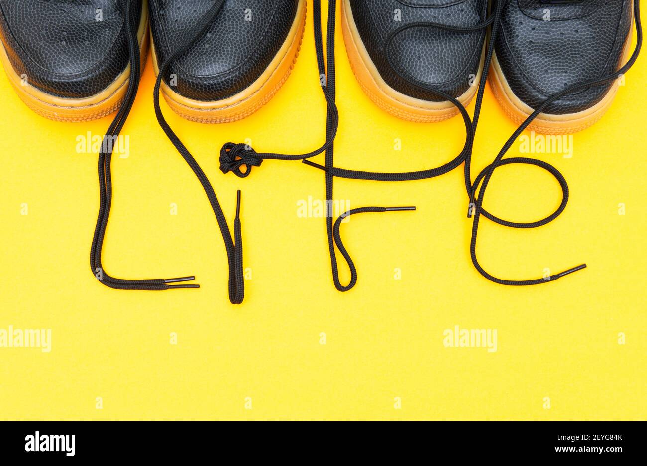 Crop view of two pairs of similar sneakers with the word LIFE made of the shoelaces on a yellow background. Stock Photo