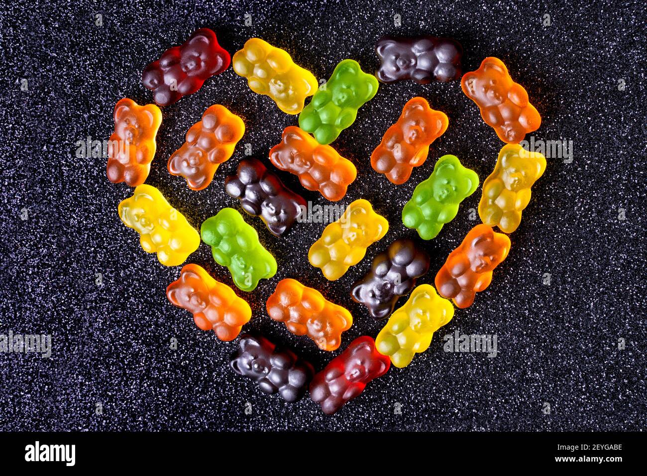 Gummy bears arranged in the shape of a heart on a sugar coated black background. Stock Photo