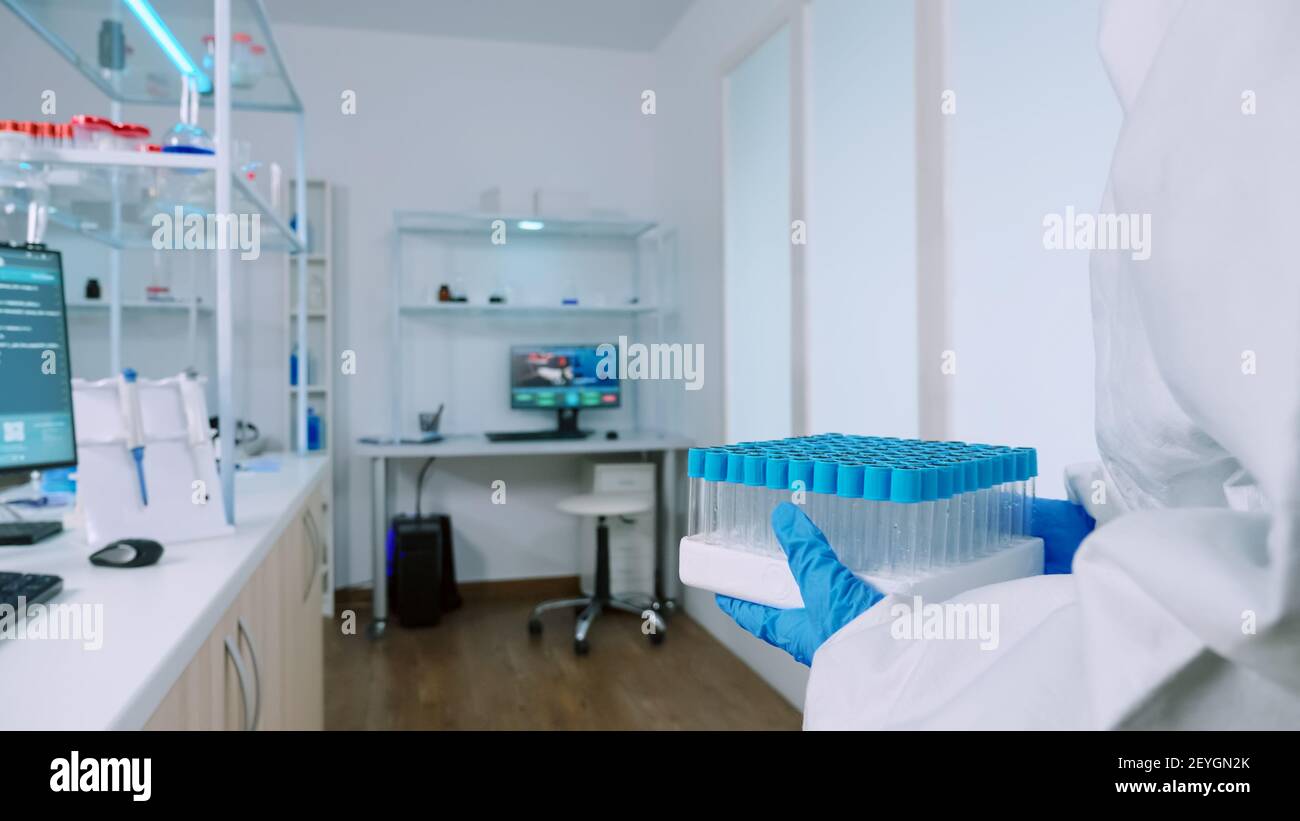 Chemist in protection suit bringing test tubes in steril laboratory and ...