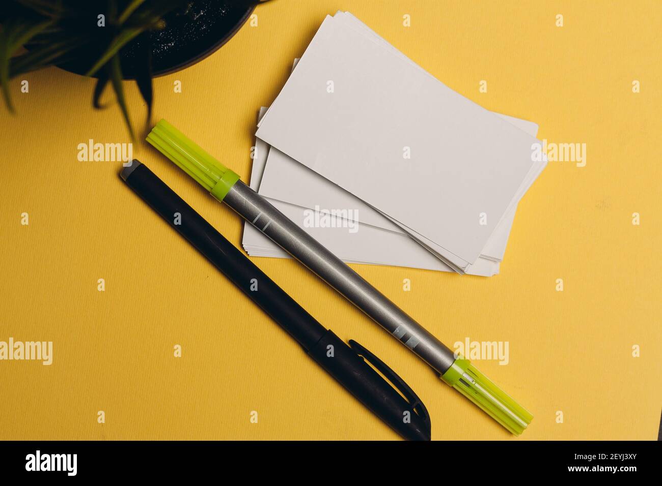 markers pens and rubber bands on a yellow background flowers in a pot and a cup of coffee Stock Photo