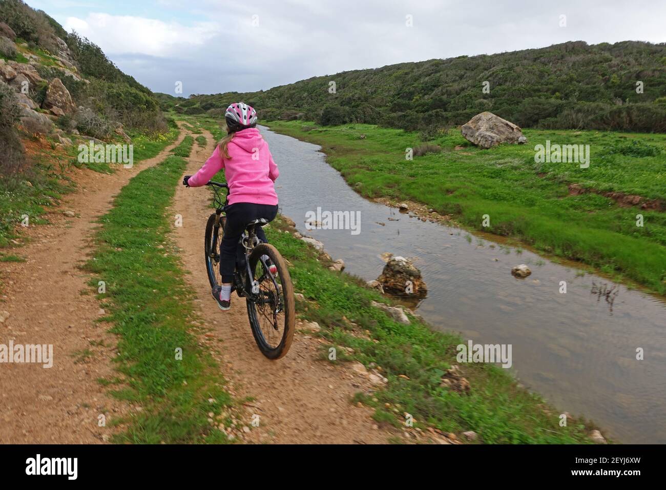 Girl on mountain bike cycling along a dirt track next to a river Stock Photo