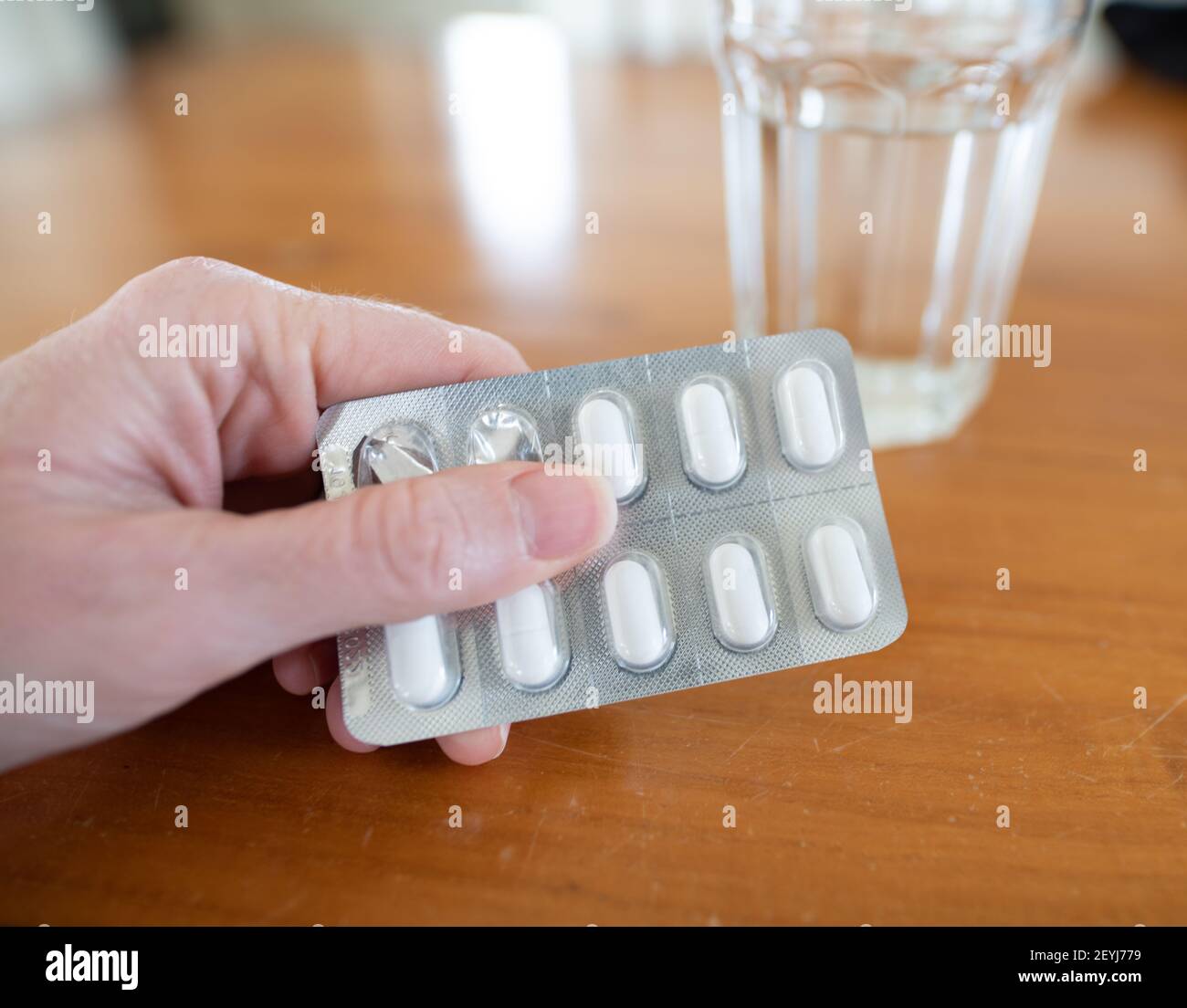 Hand holding packet of pills with glass of water in the background Stock Photo