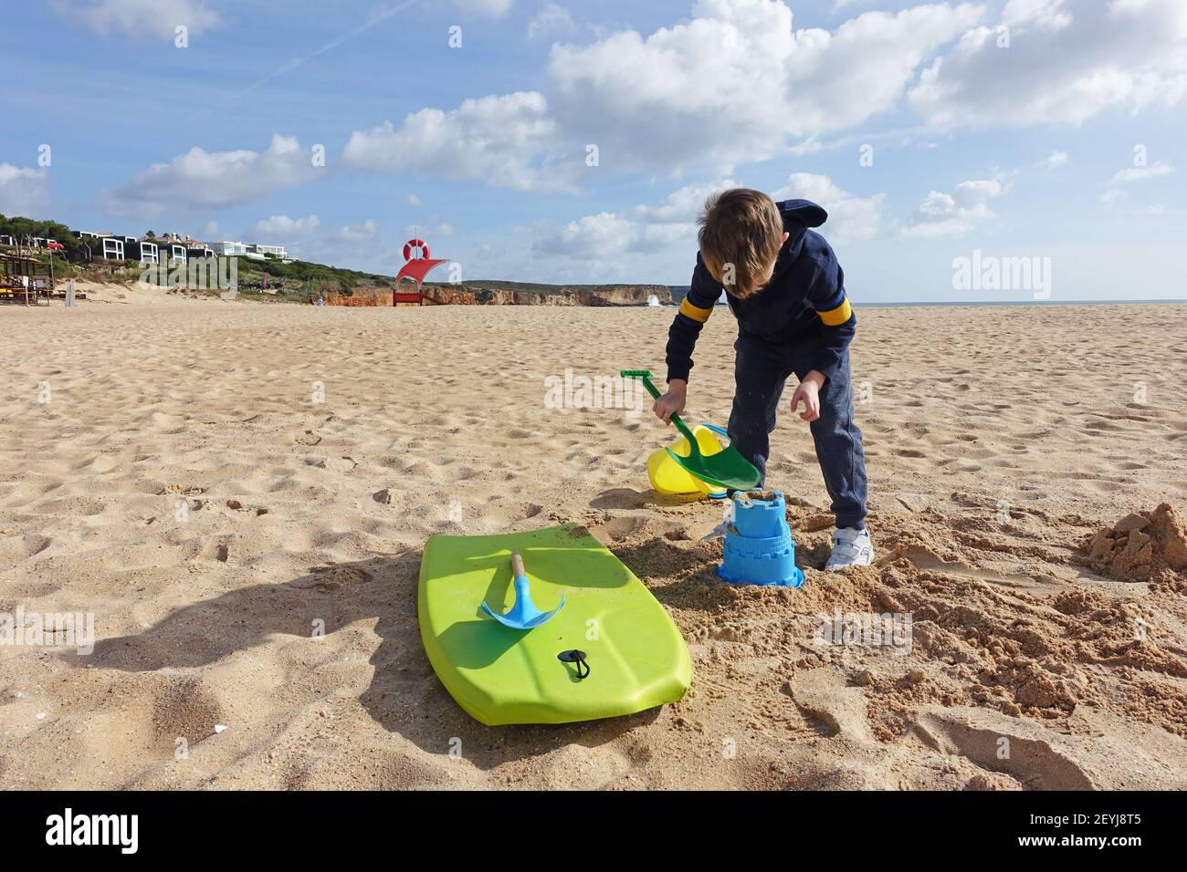 Little boy playing with a bucket and spade on the beach in winter Stock Photo
