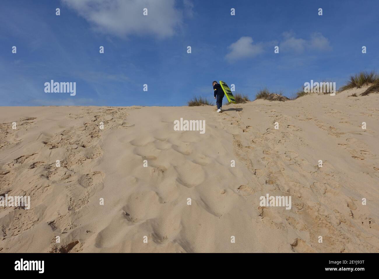 Little boy taking his boogie board to the top of the sand dunes to slide down Stock Photo