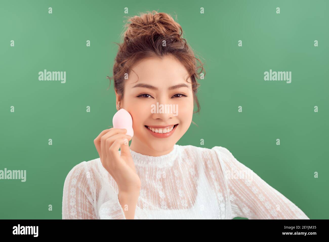 Woman applying foundation using cosmetic sponge, beauty blender. Photo of woman with perfect makeup on green background Stock Photo
