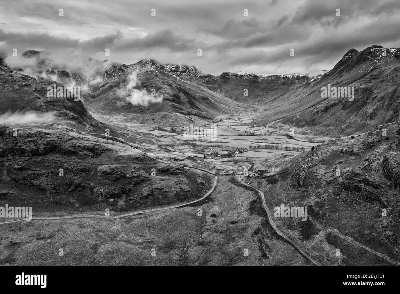 Epic flying drone  black and white landscape image of Langdale pikes and valley in Winter with low level clouds and mist swirling around Stock Photo