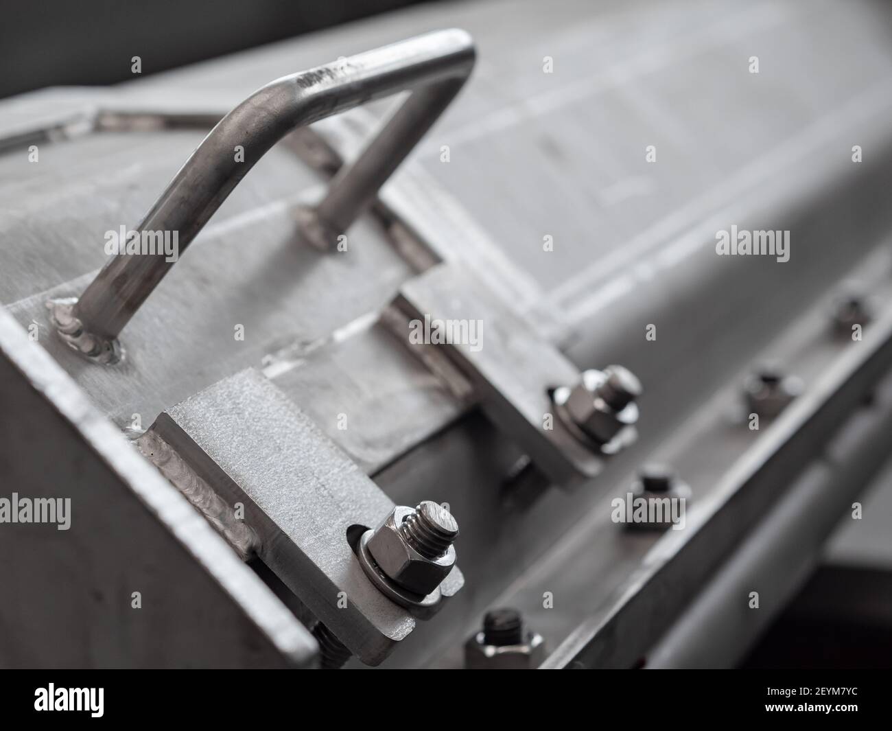 Closeup of hatch and handle of enclosed screw conveyor made from stainless steel. Shallow depth of field with the bolt in the foreground in focus. Stock Photo