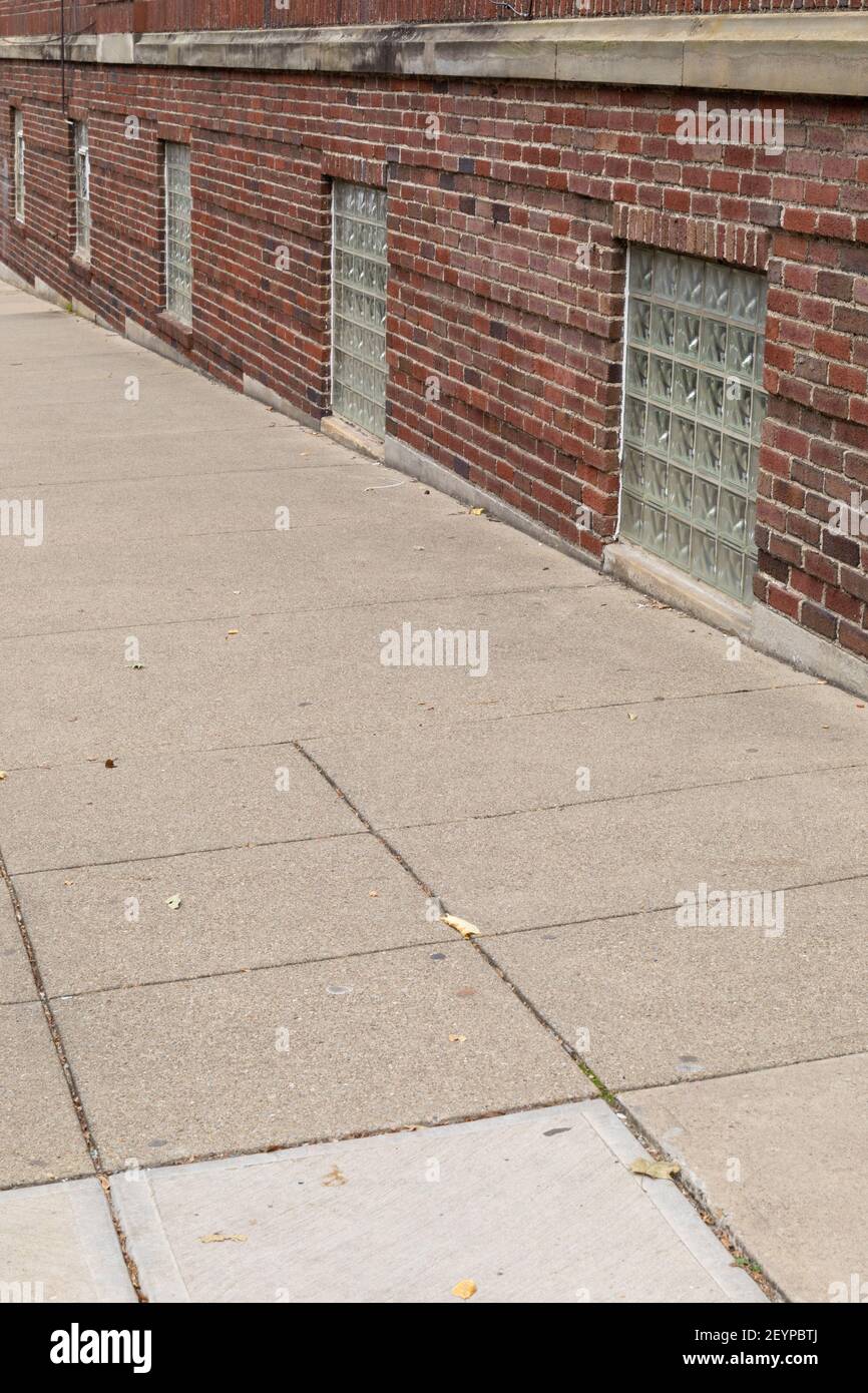 Sidewalk running directly against a red brick building with glass block