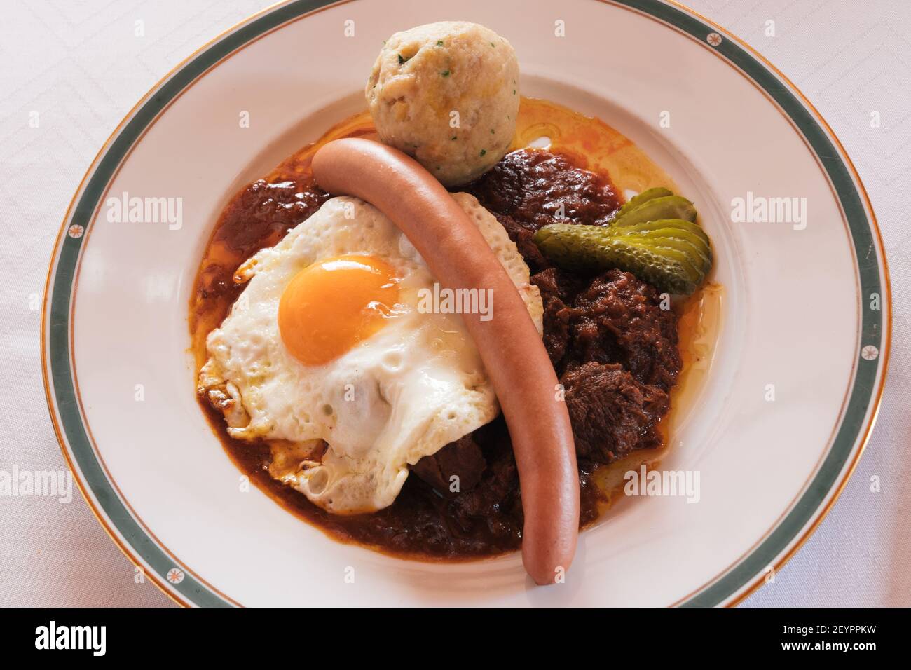 Fiakergulasch or Herrengulasch Viennese Beef Goulash Garnished with a Bread Dumpling, Frankfurt Sausage, Fried Egg and Gherkin on a Plate Stock Photo