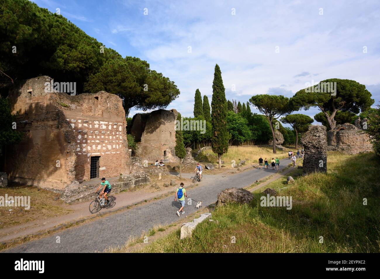 Rome Italy. Via Appia Antica (Appian Way), people walking and riding bikes amongst ancient Roman funerary monuments.   L-R; Primo Monumento in Lateriz Stock Photo