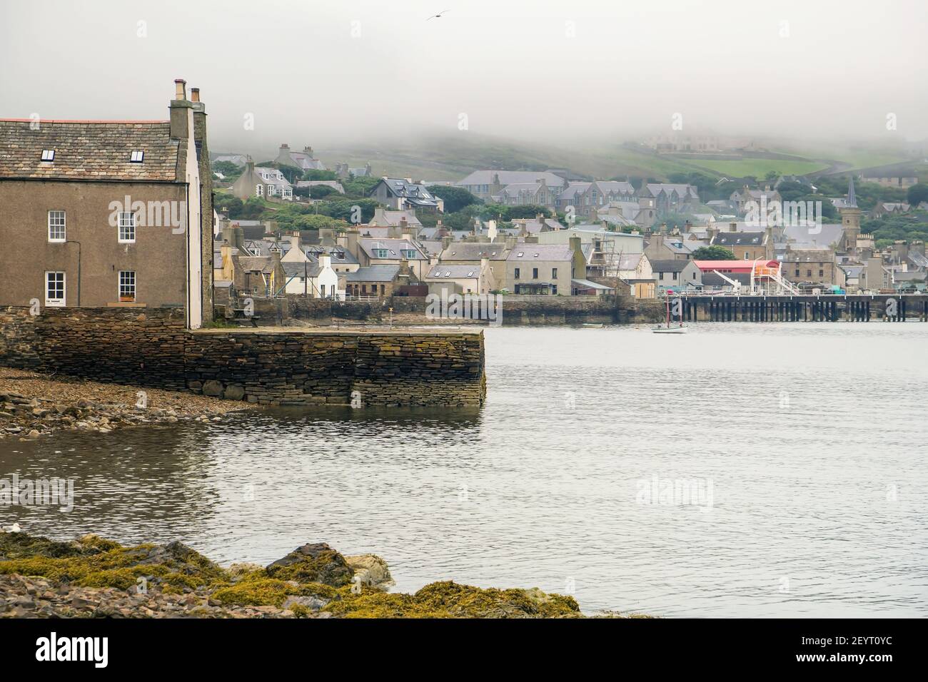 Vintage houses on waterfront view in northern Scotland on Orkney islands with shoreline in fog Stock Photo