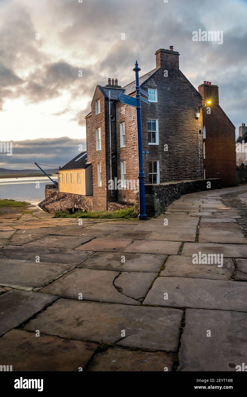 Stone slabs on scottish street with vintage house with white windows and blue sign post on Orkney islands Stock Photo