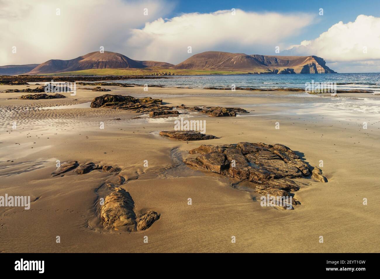 Rocks on sandy scottish beach with big hills and white clouds in background Stock Photo