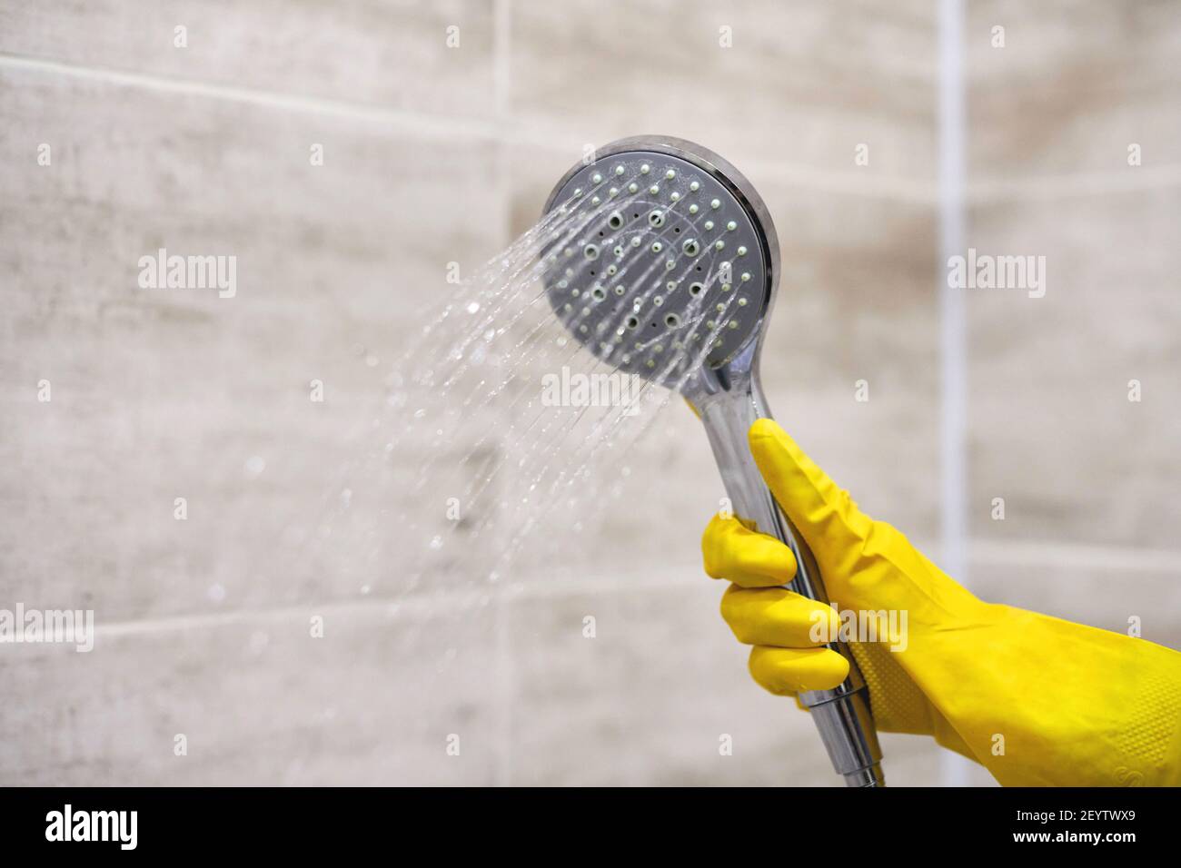 Female hand in protective yellow rubber glove holding shower head with
