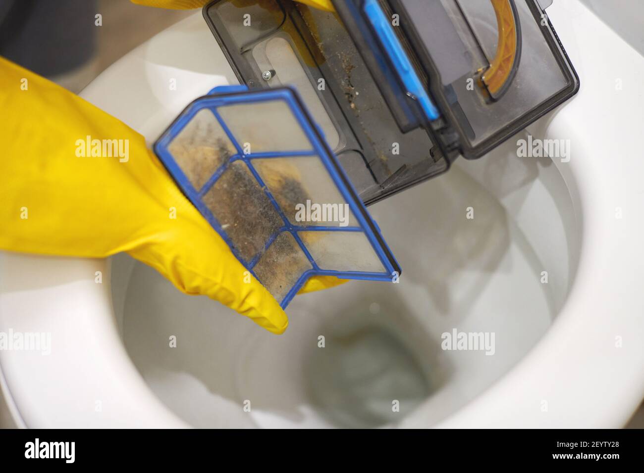 Hands in protective rubber gloves throwing trash out of robotic vacuum cleaner filter in toilet