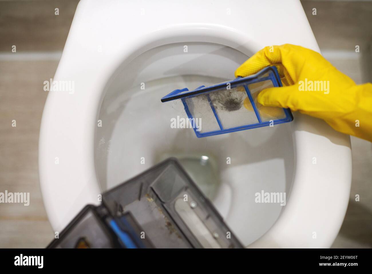Hands in protective rubber gloves throwing trash out of robotic vacuum