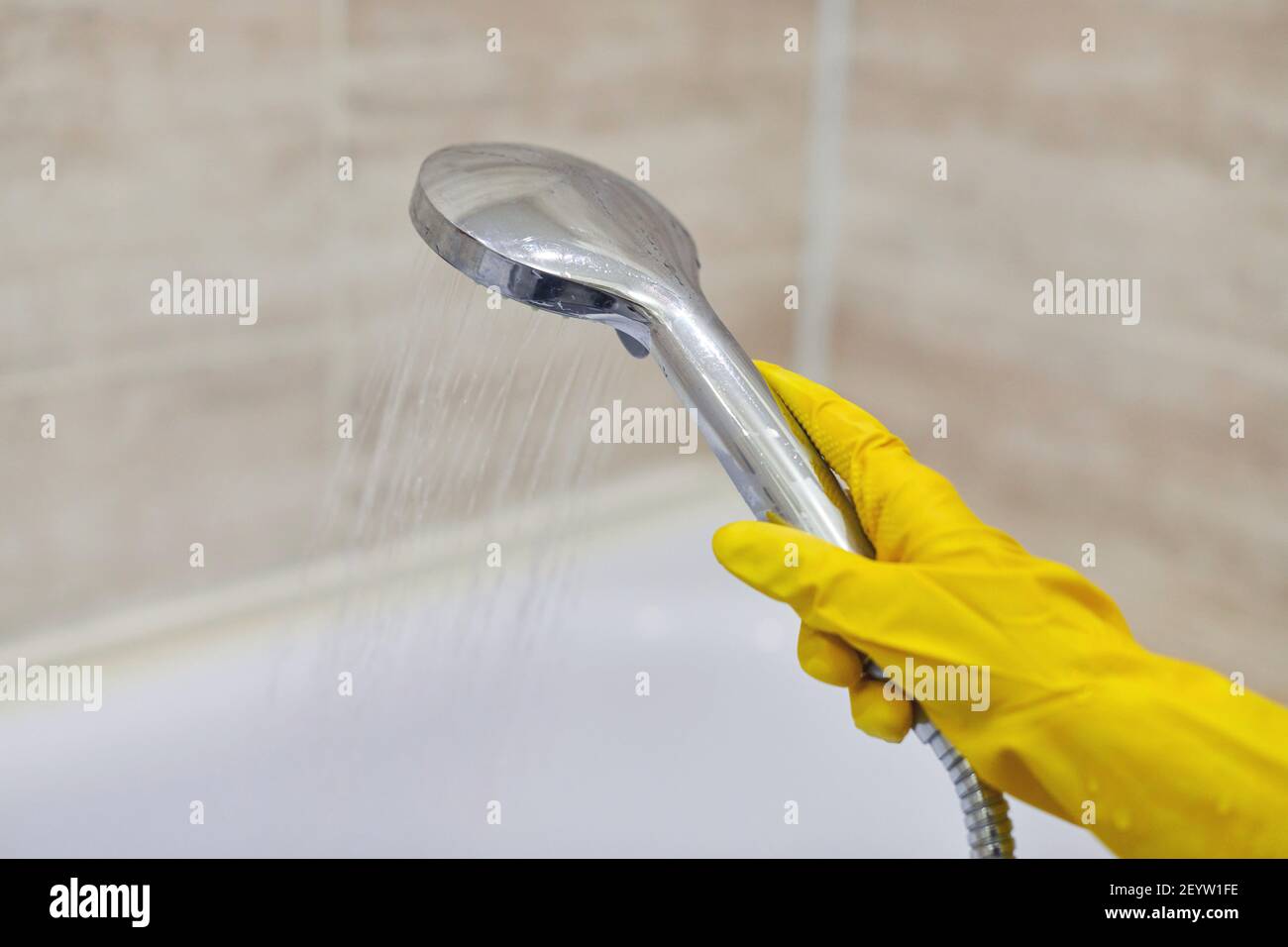 Female hand in protective yellow rubber glove holding shower head with