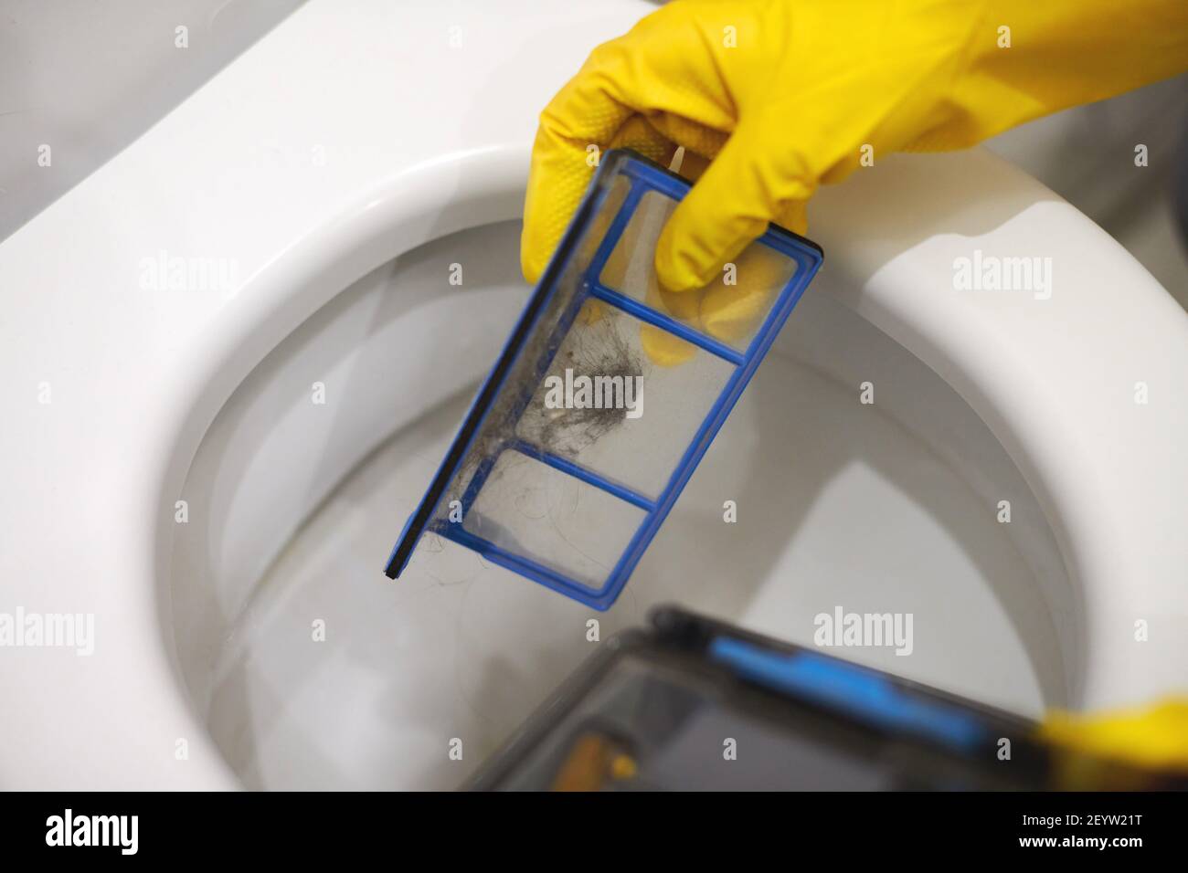 Hands in protective rubber gloves throwing trash out of robotic vacuum
