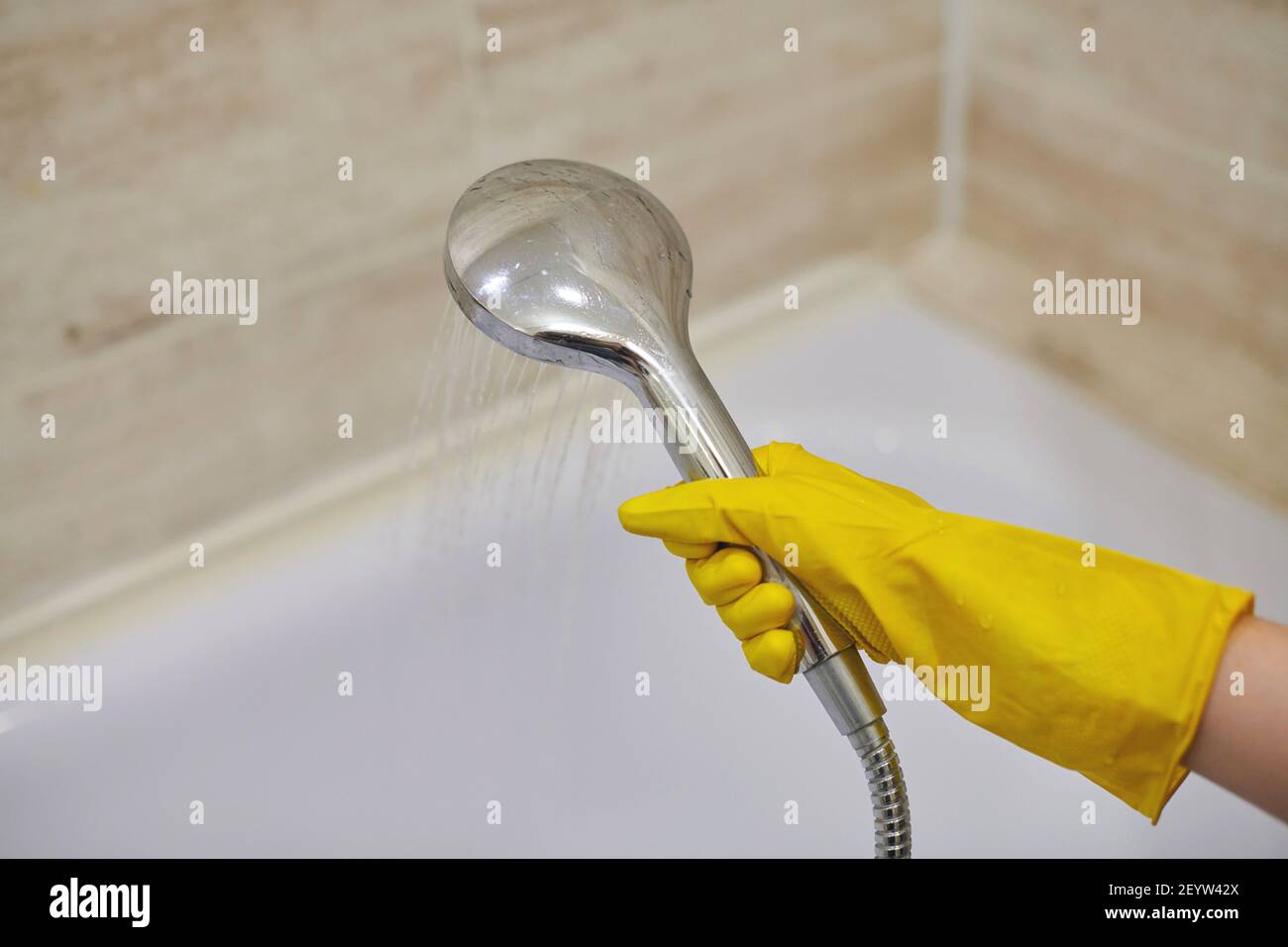 Female hand in protective yellow rubber glove holding shower head with