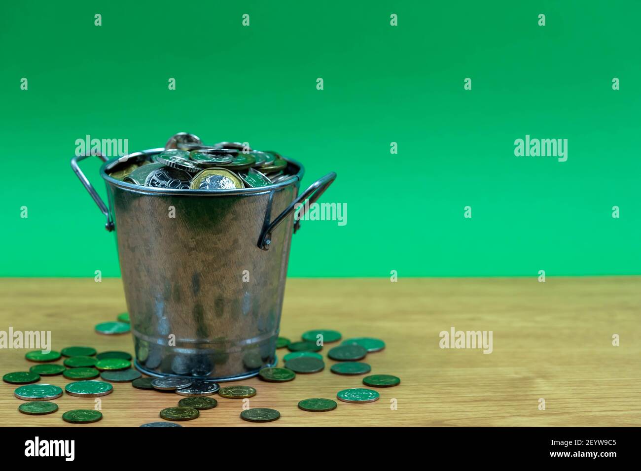 Many coins are in silver buckets on a green background. Money overflow from bucket. Coins overflow from silver bucket Stock Photo