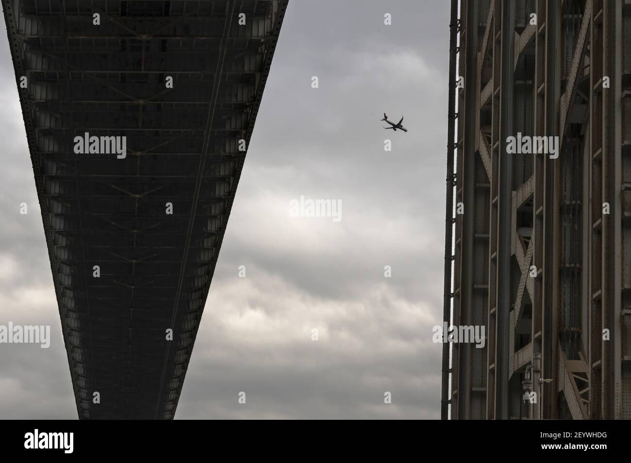 Airplane seen against a cloudy sky through the metal structure of George Washington Bridge. Stock Photo