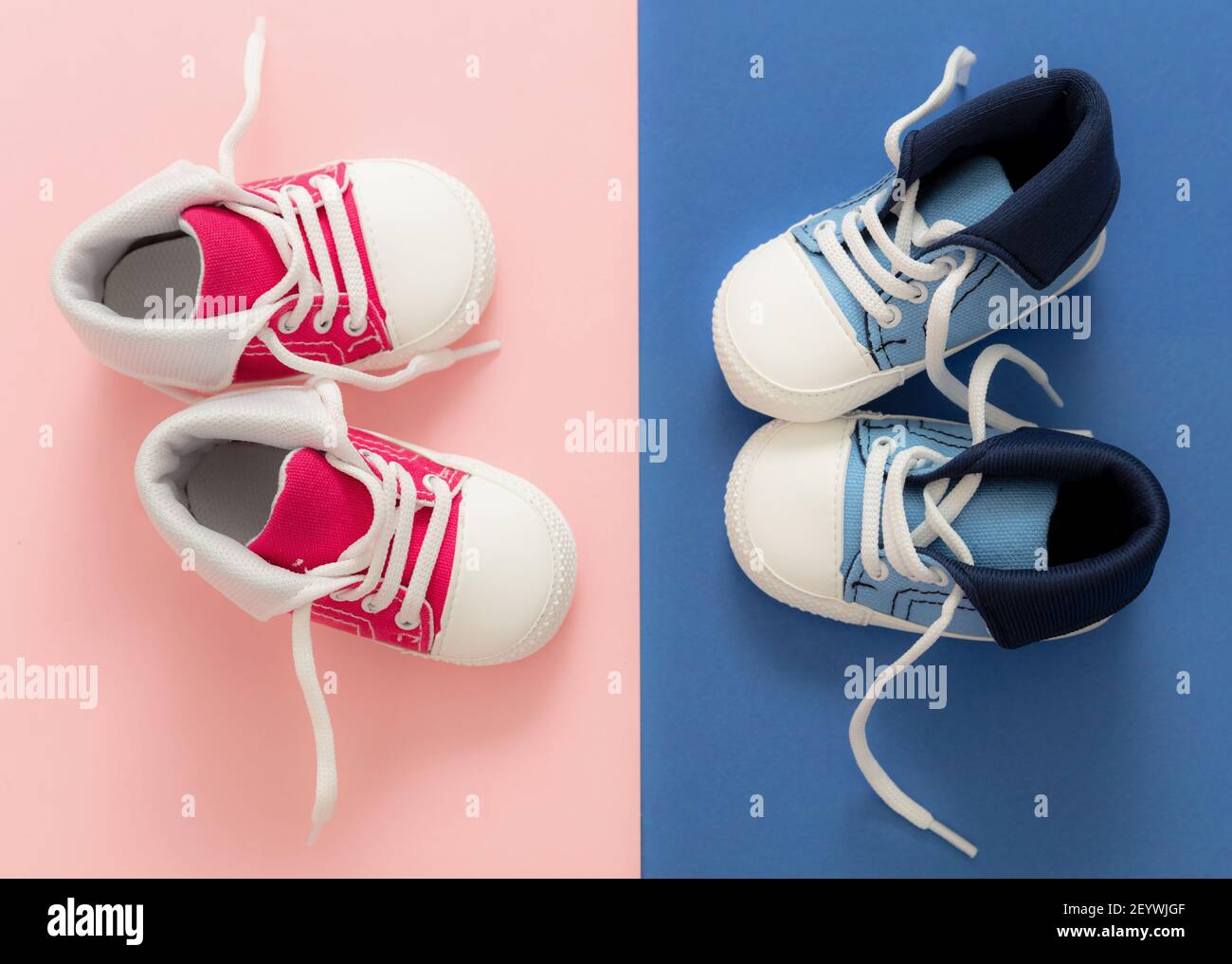 Baby boy and girl sport shoes on pastel pink and blue colors background. Red and blue kids small size sneakers, canvas booties top view Stock Photo