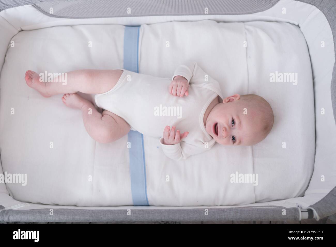 6 month old baby boy lying in his crib looking at the camera and smiling. baby products concept. Stock Photo