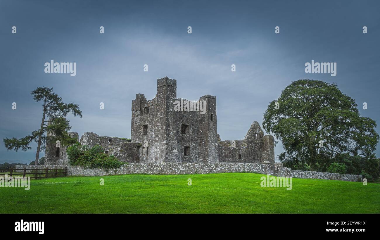 Beautiful old ruins of christian Bective Abbey from 12th century with green trees, pasture and moody dark sky in the background, County Meath, Ireland Stock Photo