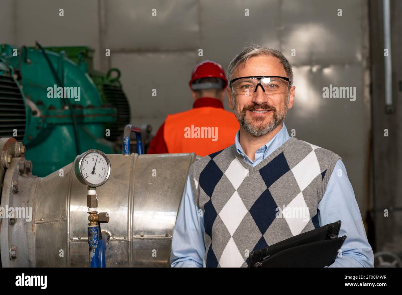 Smiling Manager With Digital Tablet Looking at Camera. Engineer Standing in District Heating Power Plant. Digital Technology Concept. Industry 4.0 Stock Photo