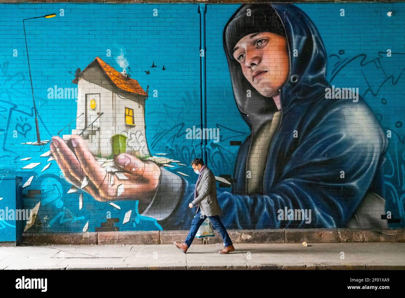 Glasgow, Scotland, UK. 6 Mar 2021. With Scotland remaining under national lockdown during the covid-19 pandemic Glasgow city centre remains a virtual ghost town with few people in the city centre and almost all shops and businesses still closed.  Pic; Man wearing facemask walks past large mural with End Youth Homelessness theme  by GW McLaughlin in the city centre. Iain Masterton/Alamy Live News Stock Photo