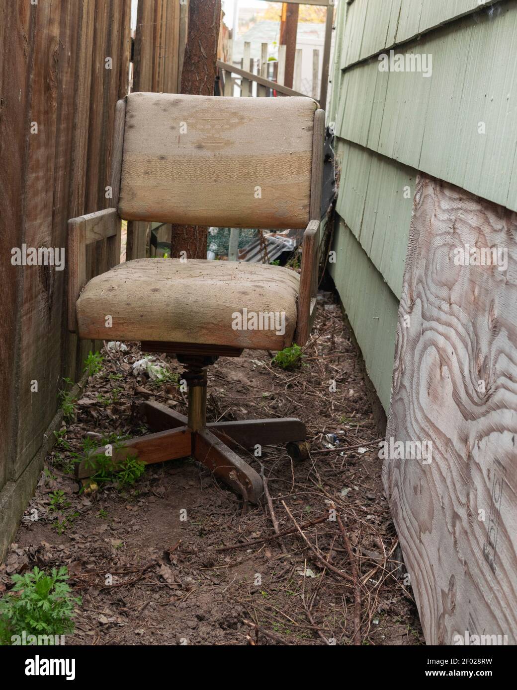 A moldy old office chair has been thrown out and now occupies a narrow space between two buildings. Stock Photo