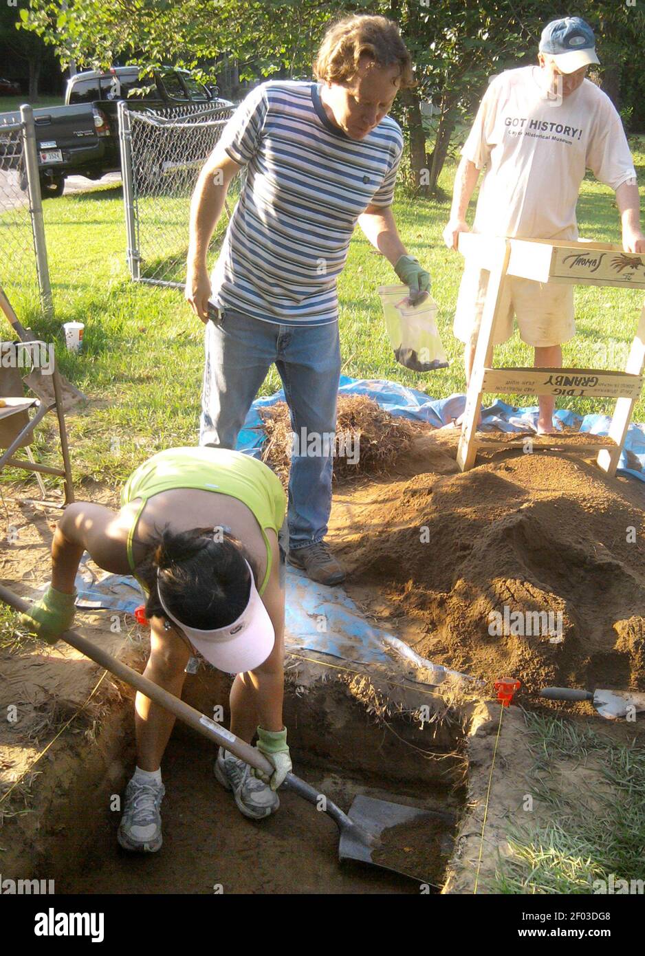 Modesta Brinkman, bottom, scrapes soil from a hole in the front yard of