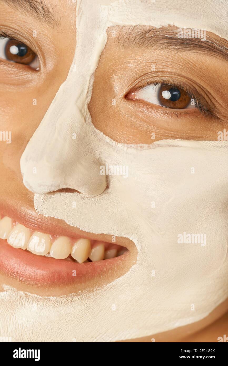 Happy young woman with facial mask applied on half of her face receiving spa treatments, smiling at camera. Beauty, skincare concept Stock Photo