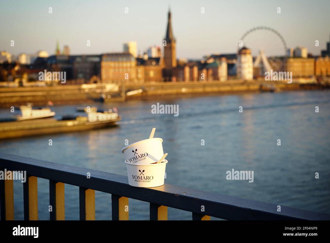 'Yomaro' frozen yogurt paper cups on the railing of Oberkasseler bridge at Rhine river. View of Old Town in the blurred background. Vignette effect. Stock Photo