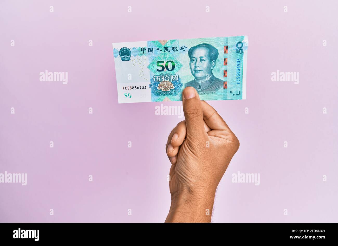 Hispanic hand holding 50 chinese yuan banknote over isolated pink background. Stock Photo