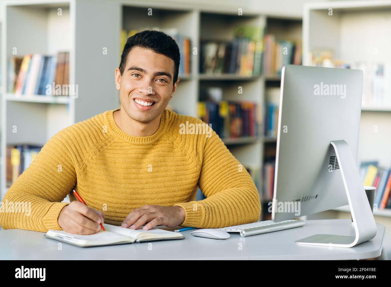 Successful hispanic male freelancer at the workplace, looks directly at the camera, smiling. Joyful handsome guy at webinar training or online conference Stock Photo
