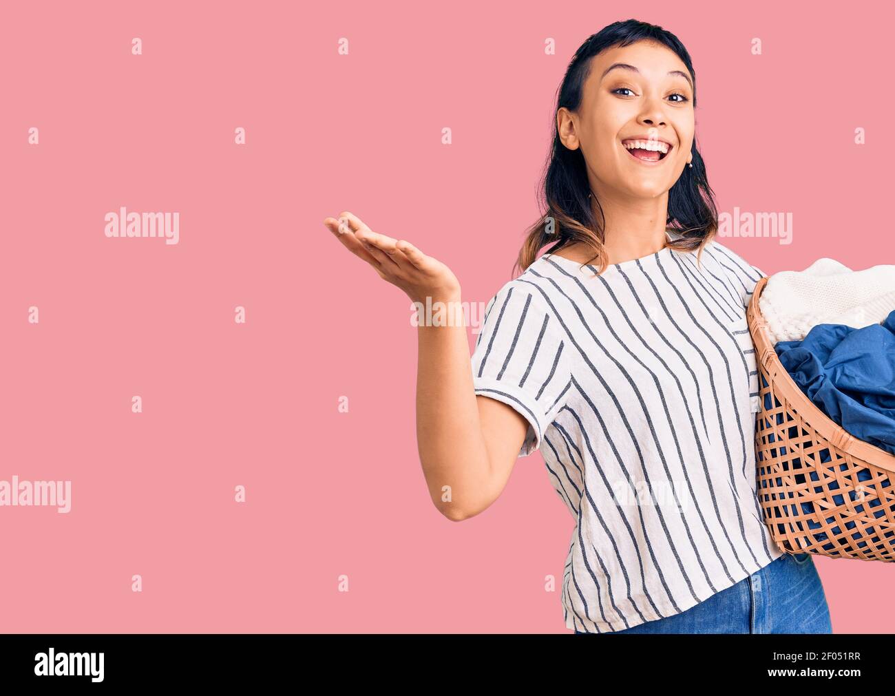Young woman holding laundry basket celebrating victory with happy smile ...