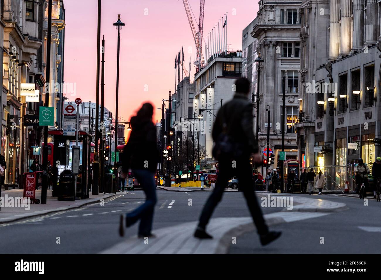 London, UK, March 6, 2021. Commuters cross Oxford Street as the sun sets over largely empty street during an ongoing third Coronavirus lockdown. Oxford Street is usually busy with crowds of shoppers. The Prime Minister Boris Johnson has set a road map on easing the restrictions. Credit: Dominika Zarzycka/Alamy Live News Stock Photo