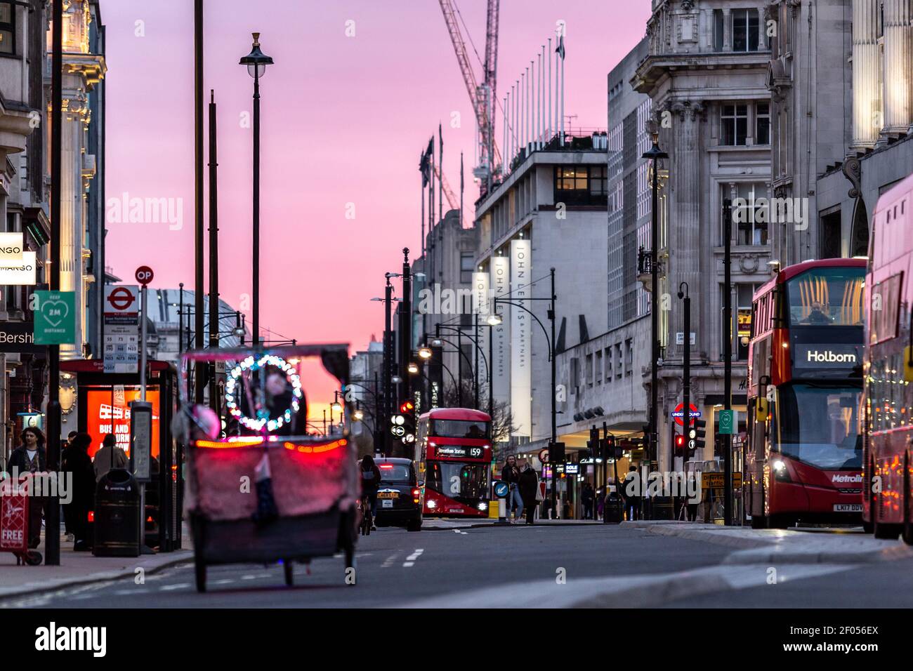 London, UK, March 6, 2021. Commuters cross Oxford Street as the sun sets over largely empty street during an ongoing third Coronavirus lockdown. Oxford Street is usually busy with crowds of shoppers. The Prime Minister Boris Johnson has set a road map on easing the restrictions. Credit: Dominika Zarzycka/Alamy Live News Stock Photo