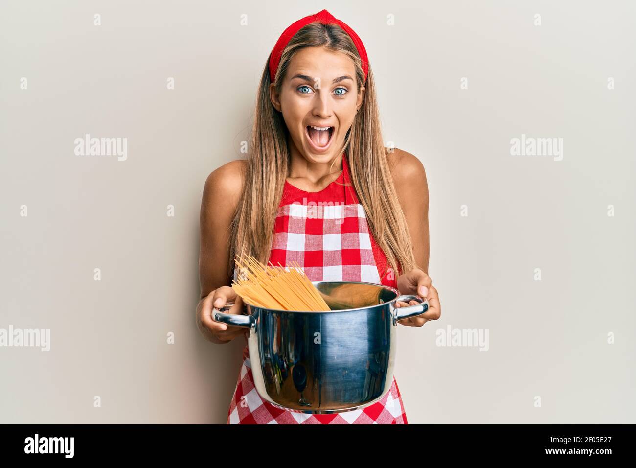 Young blonde woman wearing professional baker apron holding cooking pot with spaghetti celebrating crazy and amazed for success with open eyes screami Stock Photo