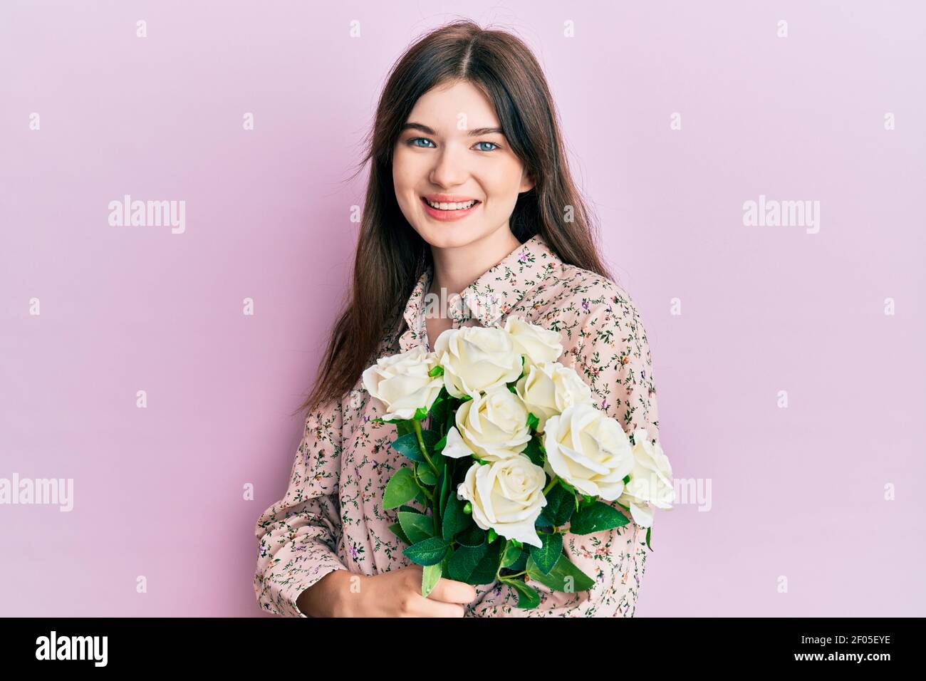 Young beautiful caucasian girl holding bouquet of white flowers looking ...