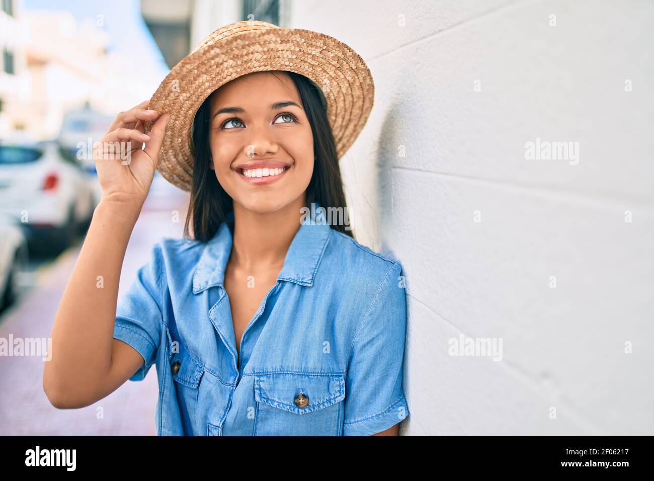 Young latin tourist girl on vacation smiling happy leaning on the wall ...