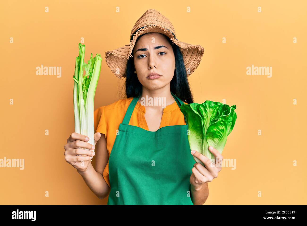 Beautiful young woman wearing gardener apron holding vegetables depressed and worry for distress