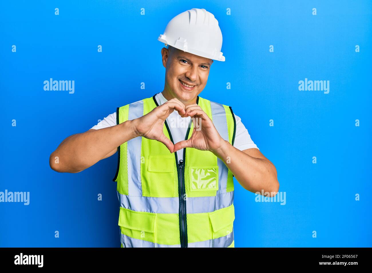 Middle age bald man wearing architect hardhat smiling in love doing