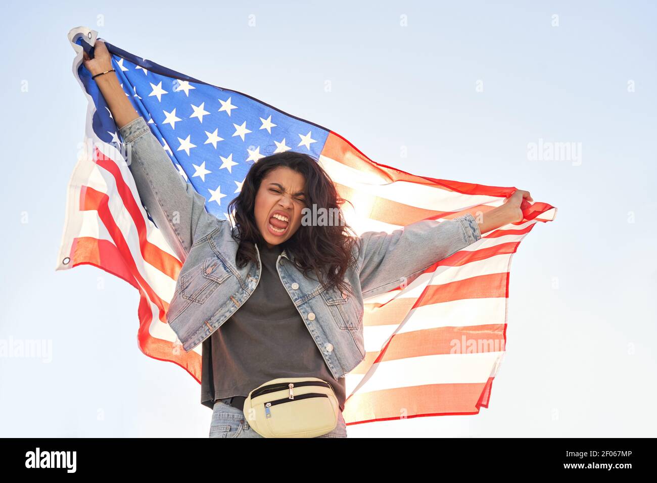 Angry young black woman screaming holding United States of America flag outdoor. Stock Photo