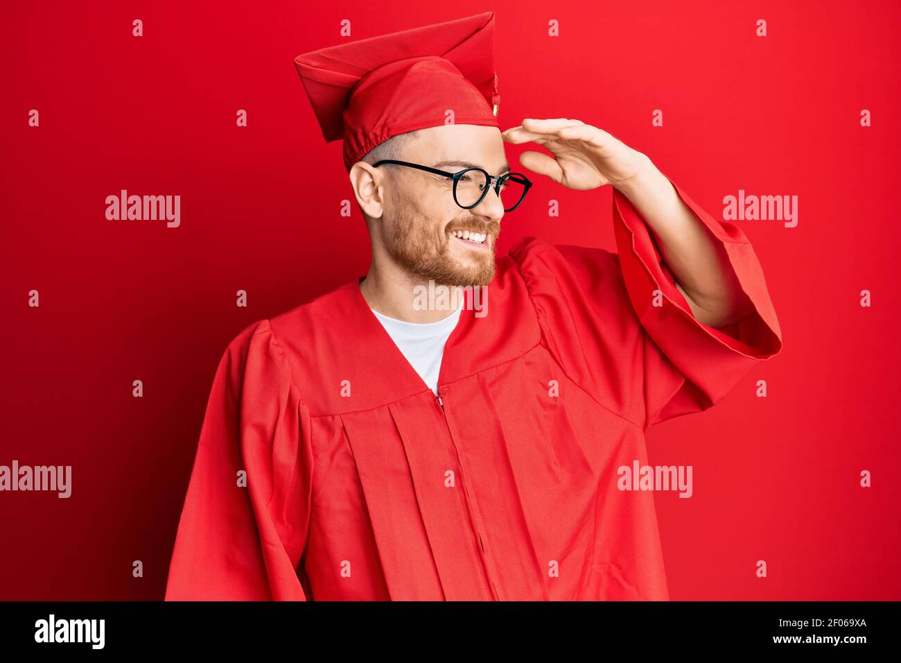 Young redhead man wearing red graduation cap and ceremony robe very ...