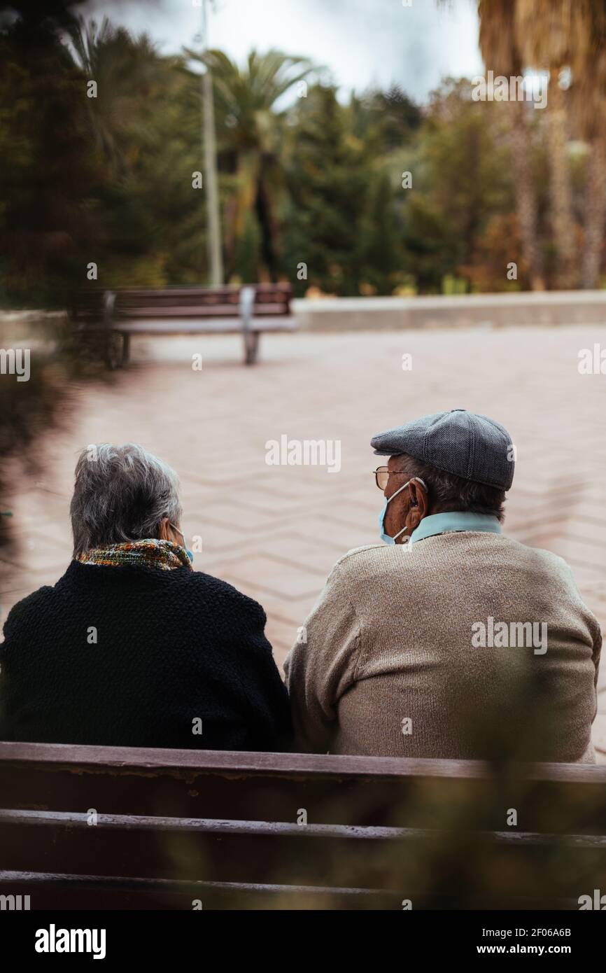 Back view of an unrecognizable elderly couple sitting on a park bench ...