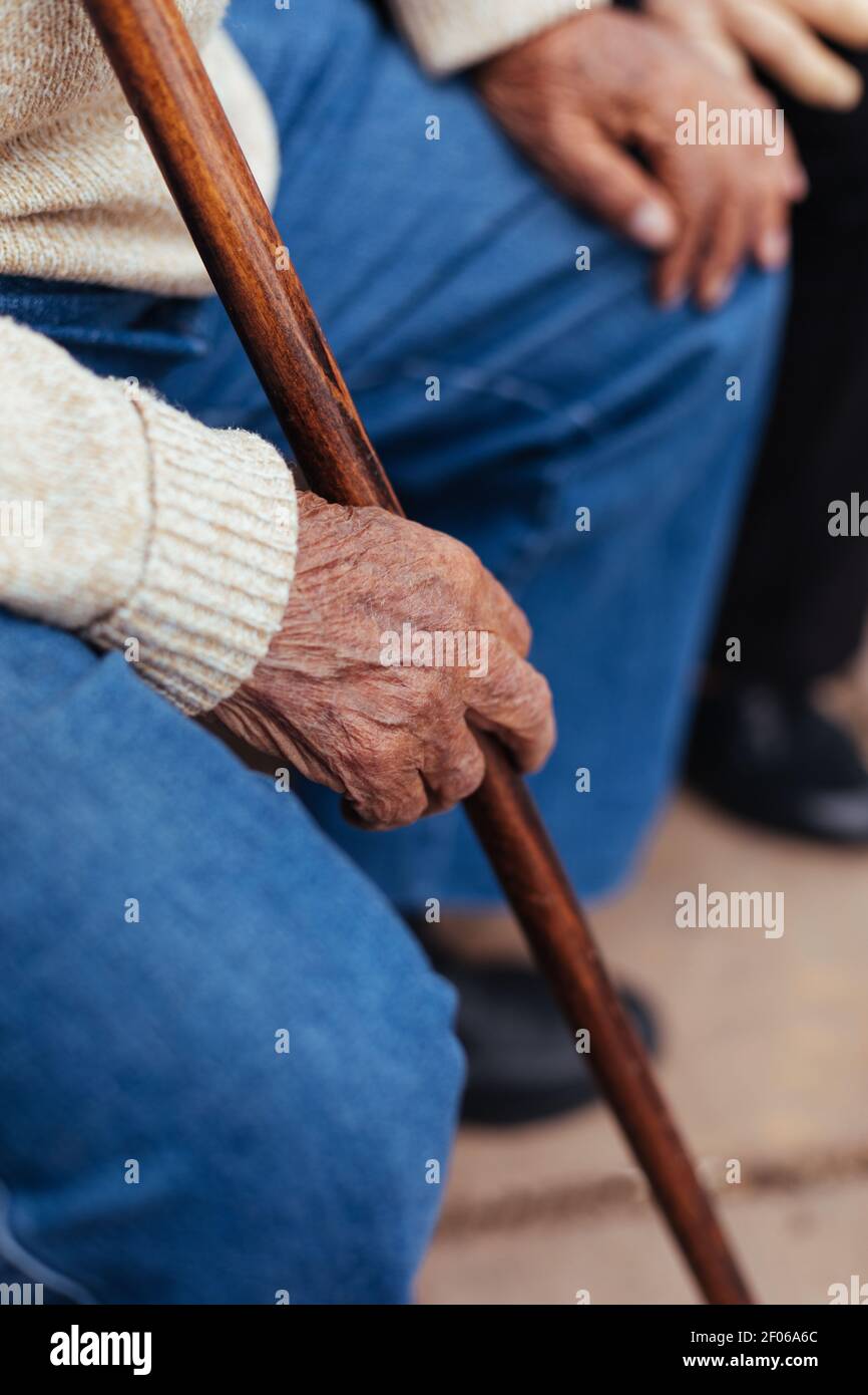 Anonymous senior person holding cane while sitting on park bench Stock Photo