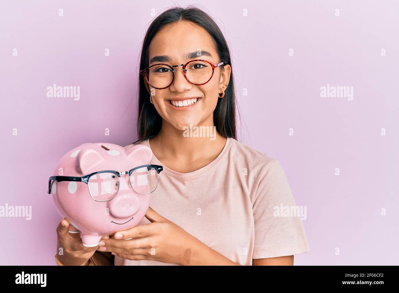 Young asian woman holding piggy bank with glasses looking positive and ...