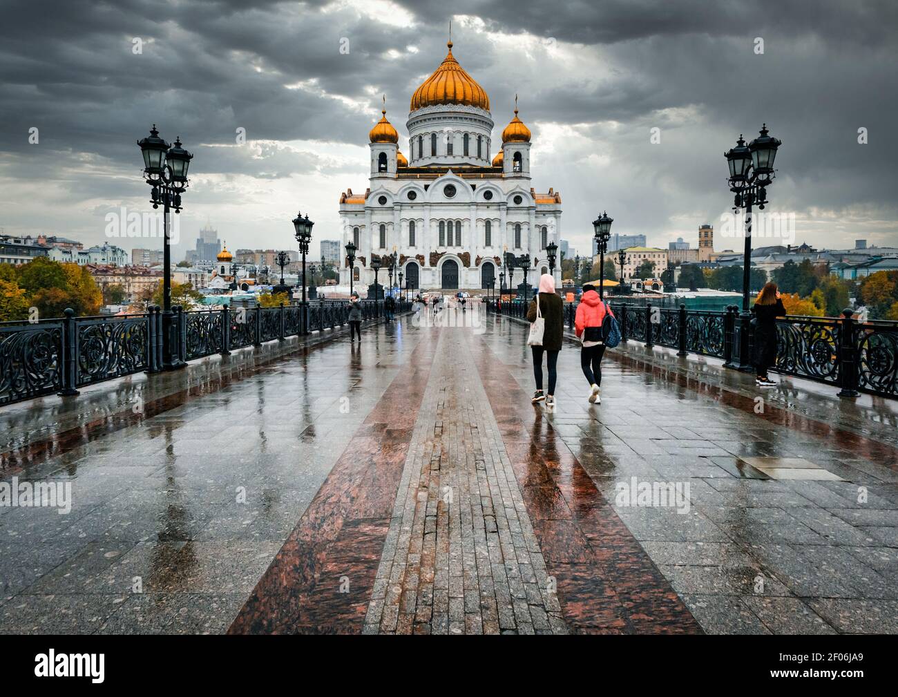 People walking in rain on Patriarshiy Bridge over Moskva River towards St Saviour's Cathedral with stormy sky. Moscow, Russia Stock Photo